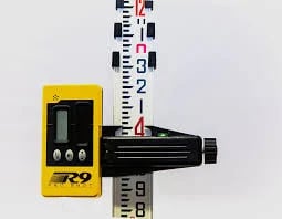 Yellow laser level tool positioned against a measuring scale ruler on white background