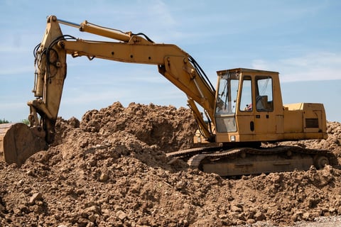 Yellow excavator digging and moving sand and dirt pile at construction site on clear blue sky day