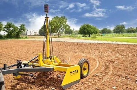 Yellow agricultural irrigation equipment on tilled soil with green fields and trees in the background under blue sky